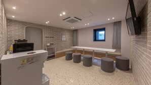 Een moderne vergaderruimte met een witte tafel, grijze krukken, een projectorscherm en een bakstenen muur.