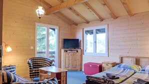 Una habitación de cabaña acogedora con una cama, una silla, una mesita, un televisor y una ventana.