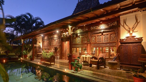 Un edificio de madera tradicional con intrincados grabados, una piscina y zona de estar al aire libre.