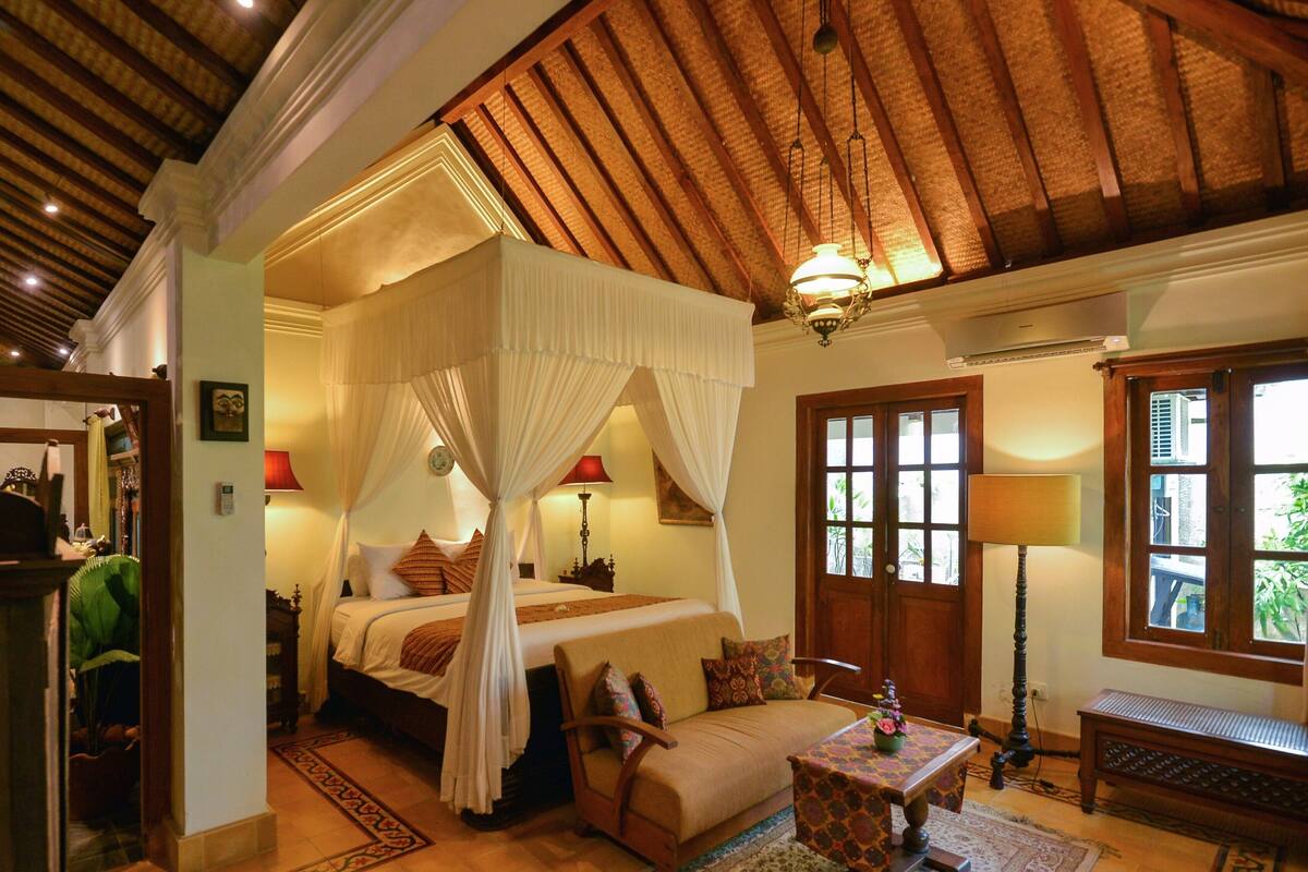 Un dormitorio con cama a dosel, una zona de estar con un banco y vistas al exterior a través de una ventana.