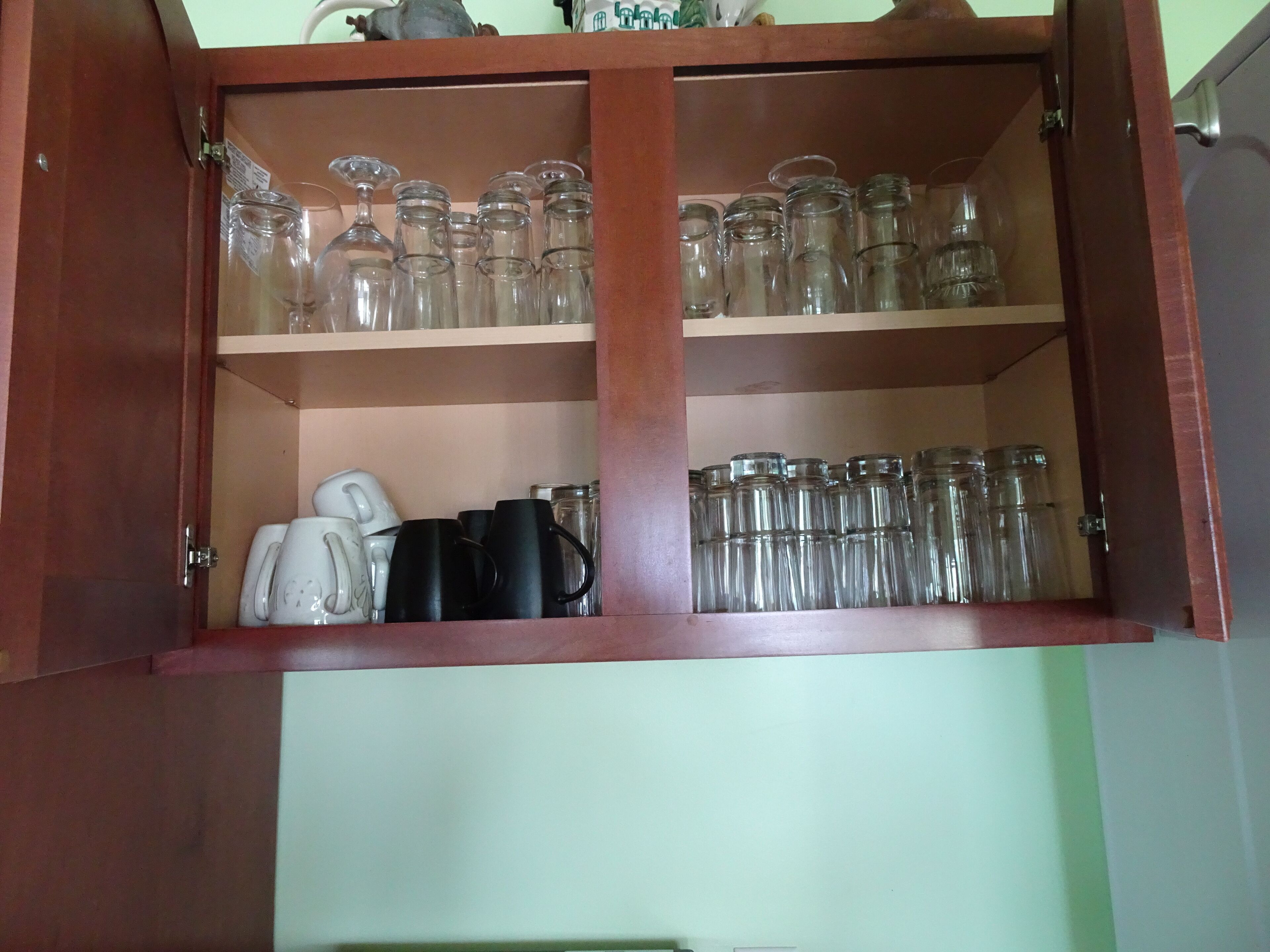 A wooden cabinet with two shelves containing glassware and mugs.