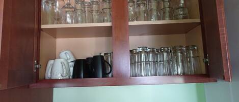 A wooden cabinet with two shelves containing glassware and mugs.