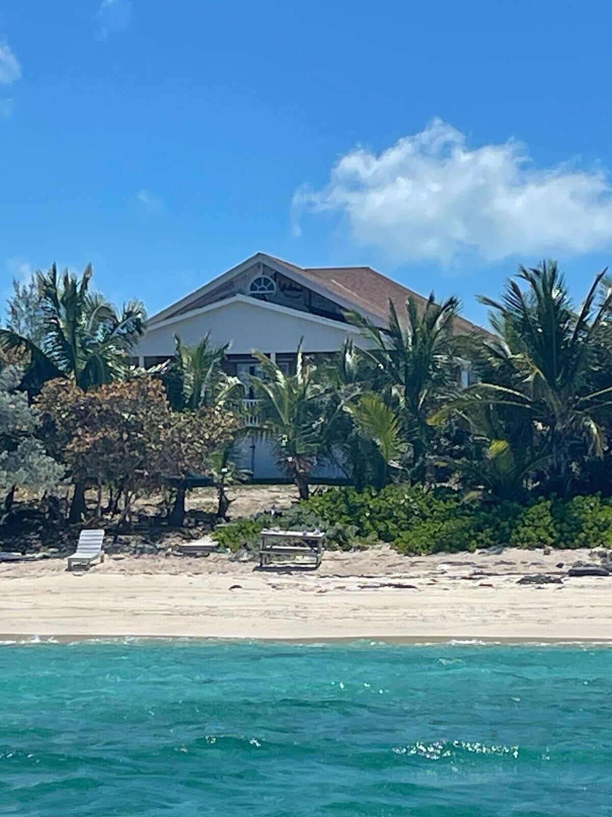 Una proprietà fronte spiaggia con una grande casa, palme e una spiaggia sabbiosa.