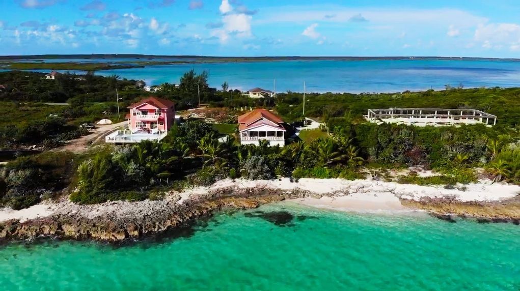 Vista aérea de una propiedad costera con una playa, una casa grande y un edificio blanco con balcón.