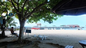 A beach with a wooden structure, a tree, and a sign. - Borneo Divers Mabul Resort (Mabul Island)
