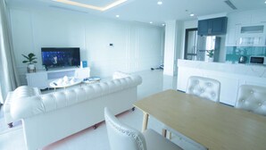 Ein modernes Wohnzimmer mit einem weißen Sofa, einem Esstisch und einer Küchenzeile mit weißen Schränken und einer Arbeitsplatte.