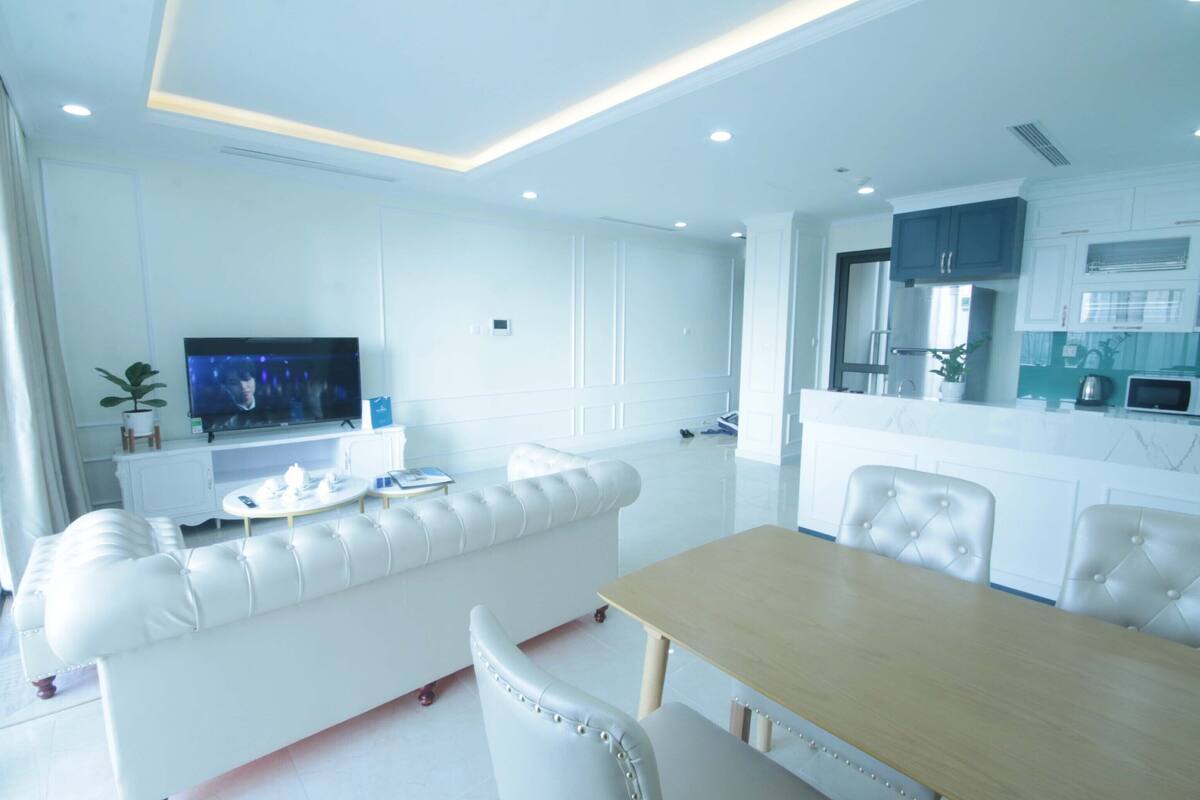 Een moderne woonkamer met een witte bank, een eettafel en een keuken met witte kasten en een aanrecht.