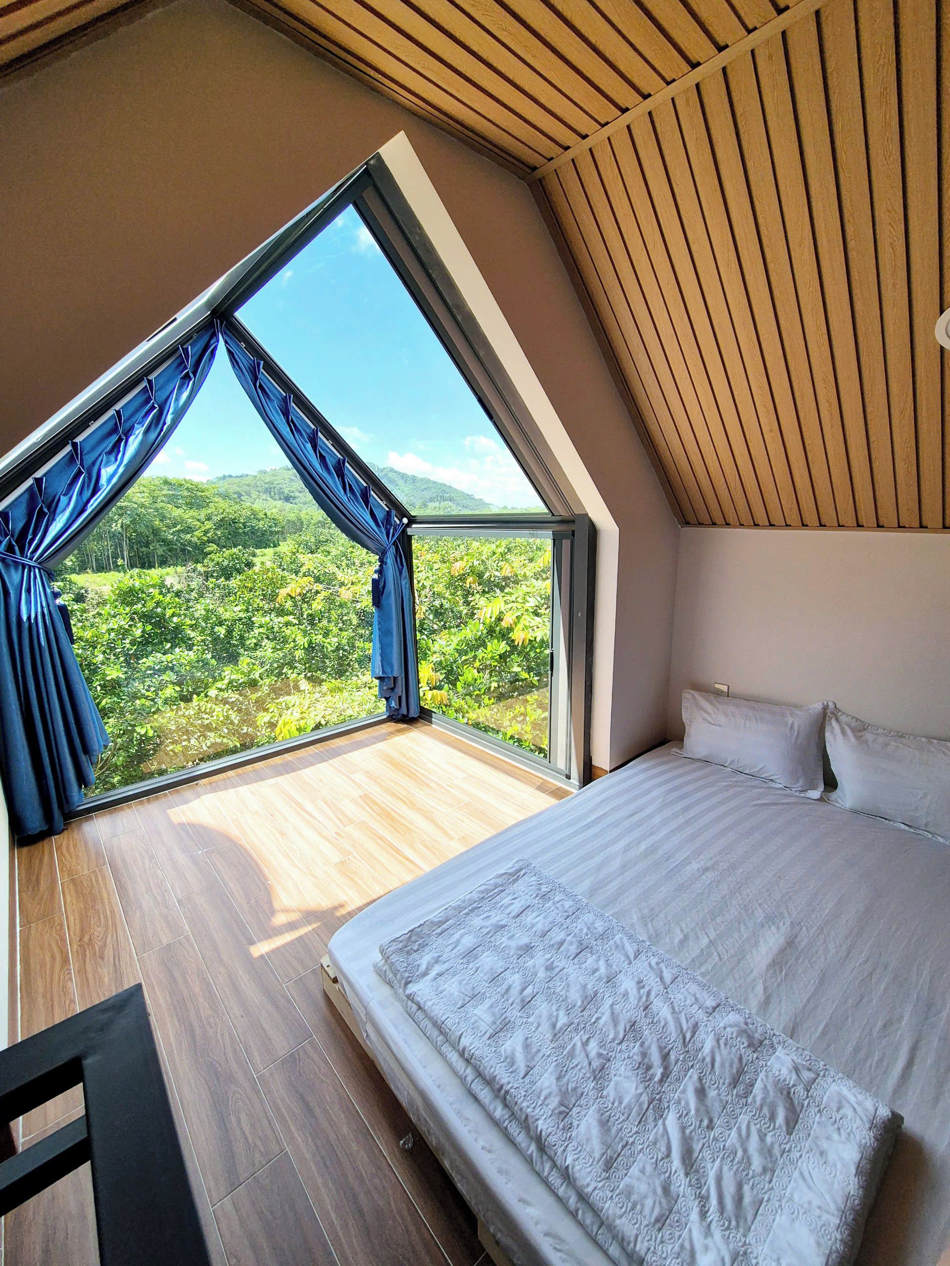 Ein Schlafzimmer mit großem Fenster, einem Bett und Blick auf einen Wald.