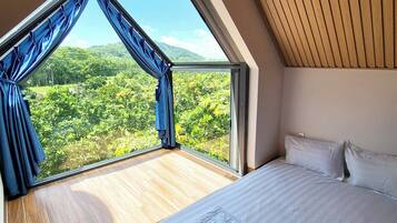 Ein Schlafzimmer mit großem Fenster, einem Bett und Blick auf einen Wald.