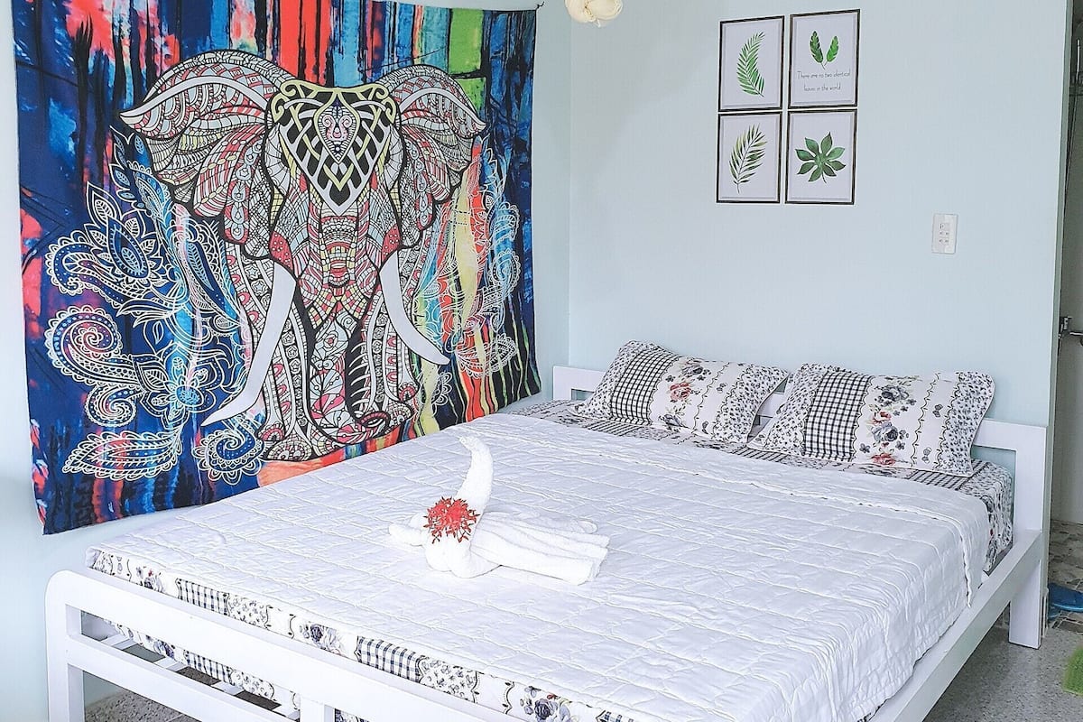 A bedroom with a bed, a colorful tapestry, and framed botanical prints on the wall.