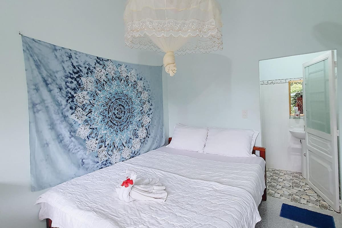 A bedroom with a bed, a tapestry, a ceiling fan, and a bathroom visible through an open door.