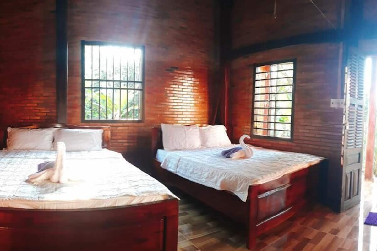 A rustic room with two wooden beds, a brick wall, and a window with bars.