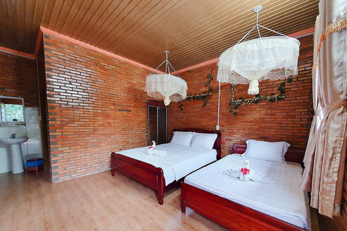 A room with two wooden beds, a brick wall, a wooden ceiling, and a hanging white canopy.