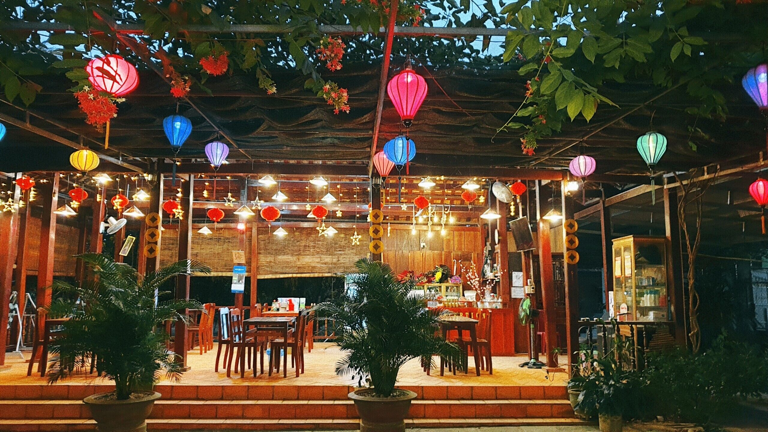 An outdoor dining area with wooden tables and chairs, surrounded by potted plants.
