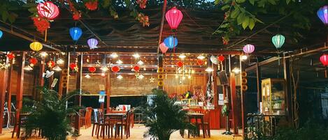 An outdoor dining area with wooden tables and chairs, surrounded by potted plants.