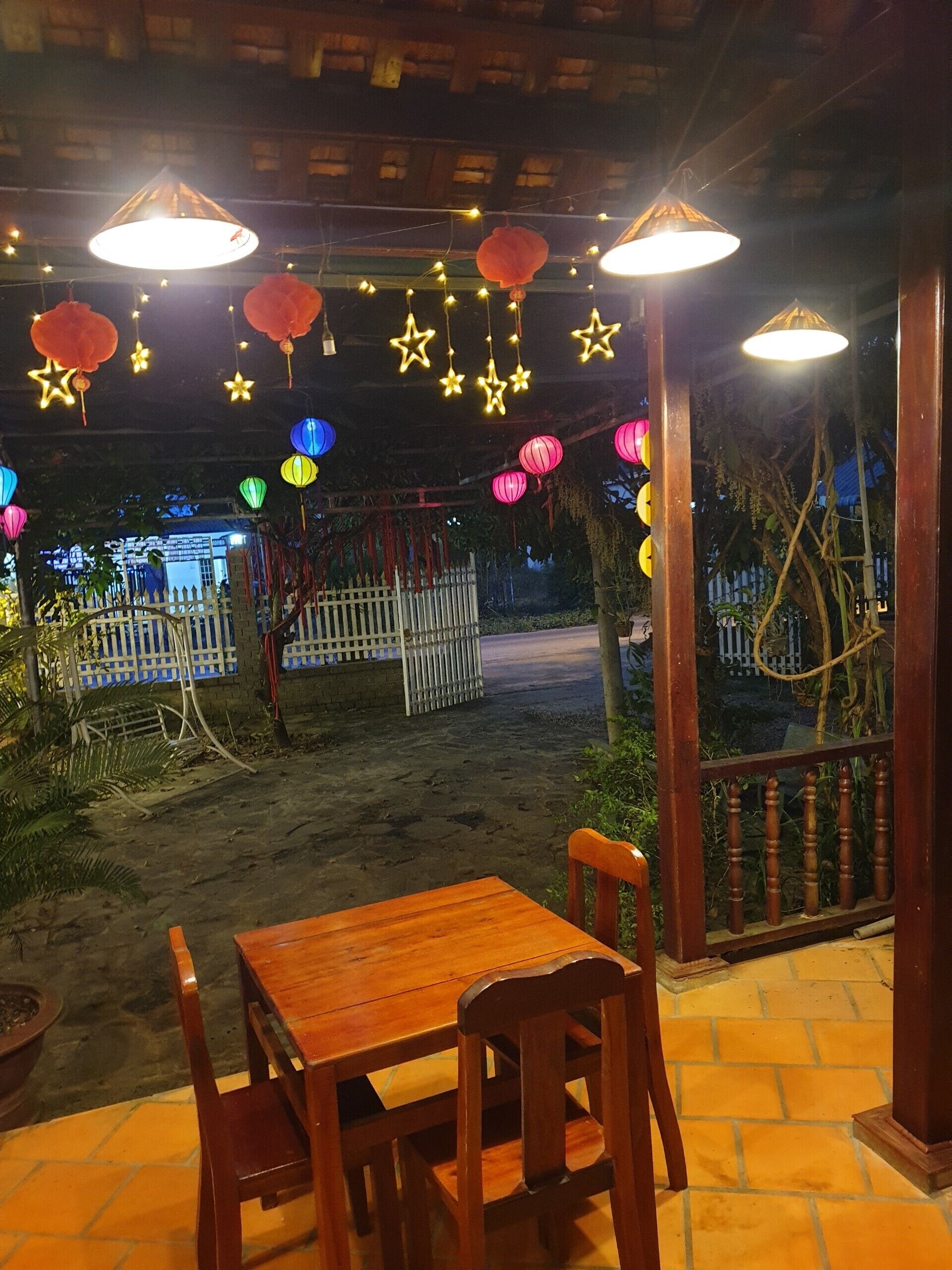 Un patio al aire libre con una mesa y sillas de madera, luces colgantes y faroles.