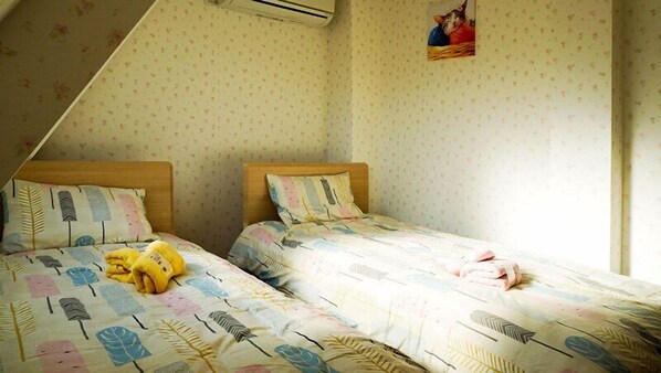 Une chambre avec deux lits simples, chacun doté d’une couette à motifs de feuilles, d’une tête de lit en bois et d’un petit tableau accroché au mur.