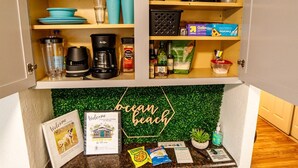 A kitchen with a wooden upper shelf holding various kitchen items, a lower shelf with a coffee maker, and a welcome sign on the countertop. - End of Summer Savings by the beach at Green Door! (San Diego)