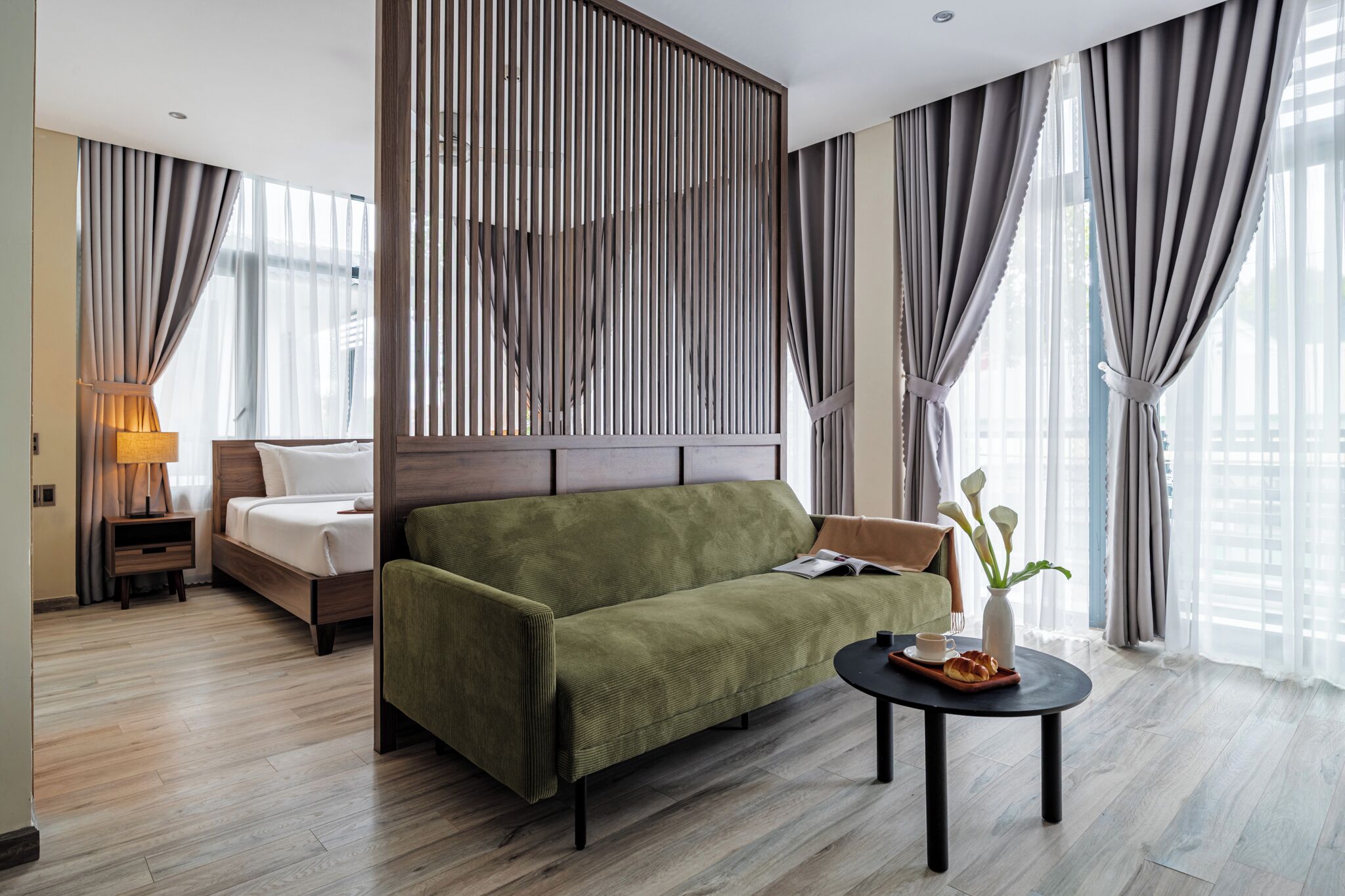Een moderne hotelkamer met een groene bank, een houten hoofdbord, een klein tafeltje met dienblad en een lamp.