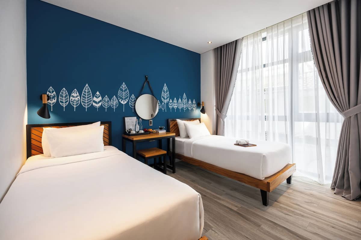 Habitación de hotel con dos camas, un escritorio, un espejo y vistas al exterior.