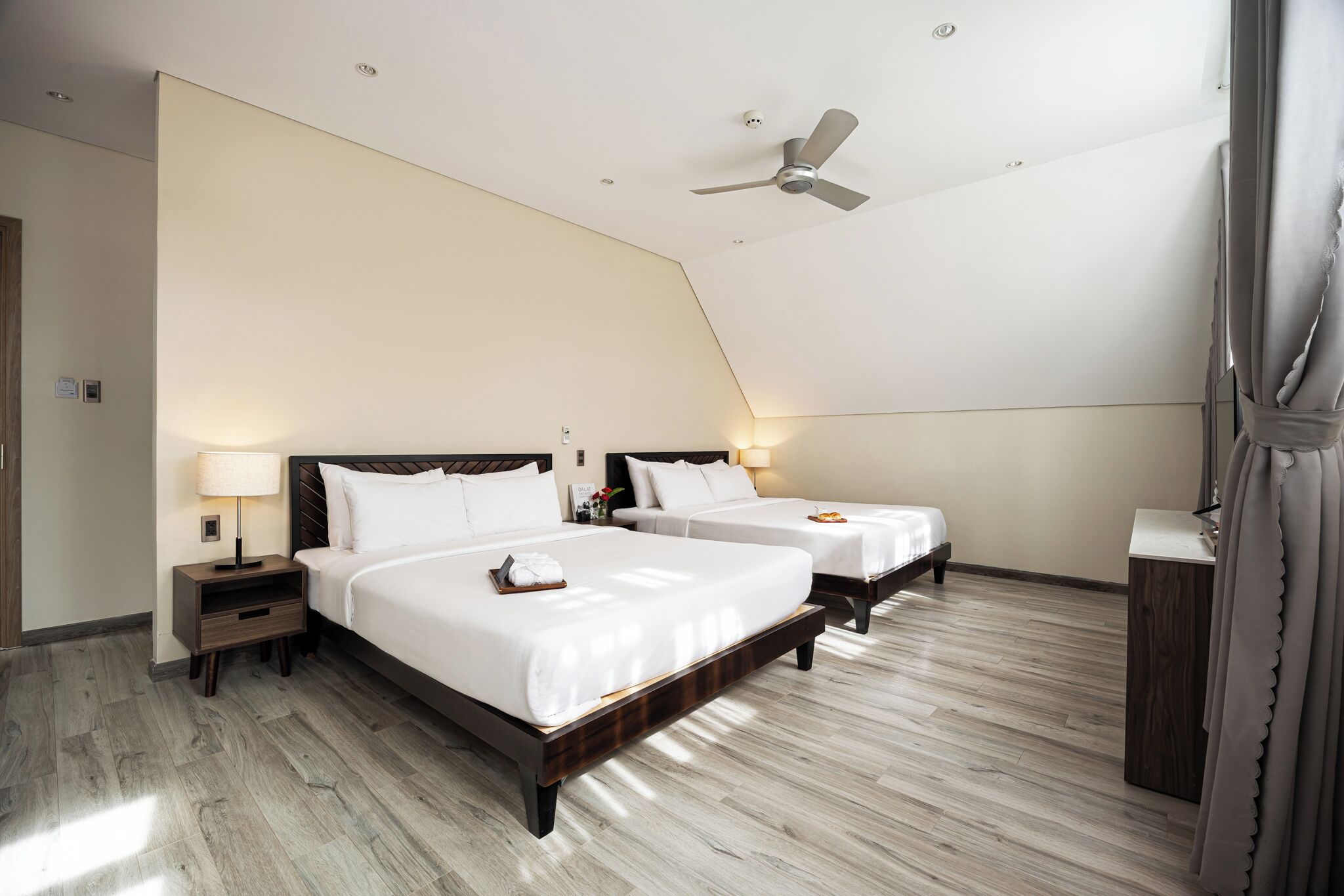 Habitación de hotel con dos camas, un ventilador de techo y un escritorio pequeño.