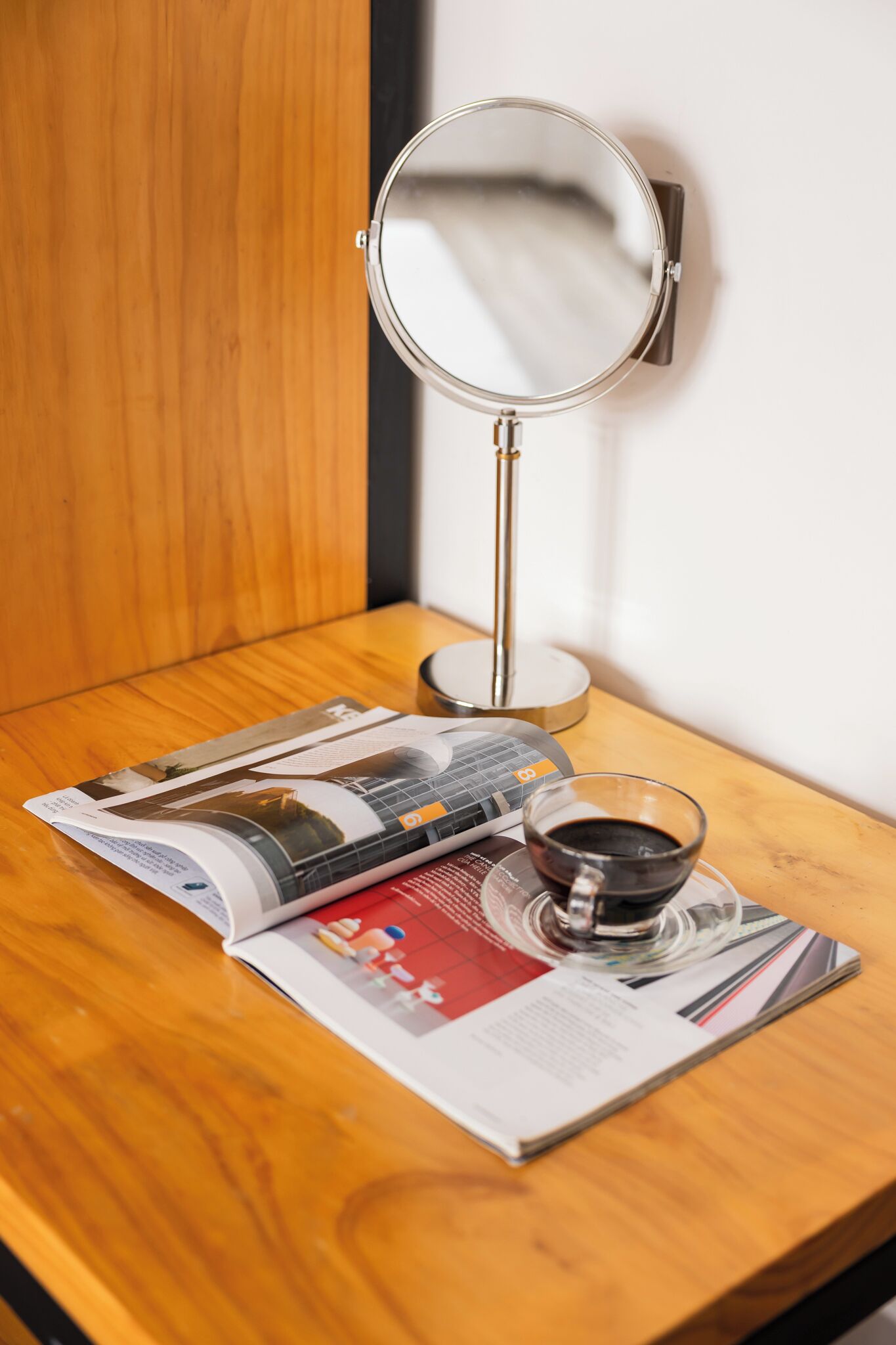 A wooden table with a magazine, a cup of coffee, and a wall-mounted mirror.