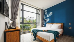 Un dormitorio con un ventanal grande, una cama con ropa de cama blanca, una mesita de noche de madera y una pared azul decorativa.