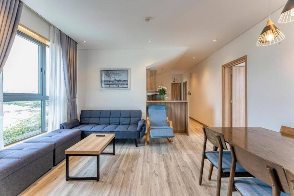 Una sala moderna con un sofá, una mesa de centro de madera y una mesa de comedor con sillas. Se observa una zona de cocina al fondo.