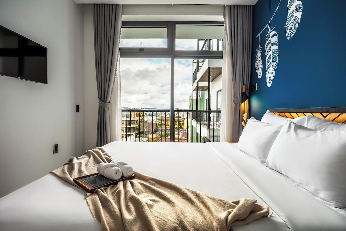 Habitación de hotel con una cama grande, un televisor montado en la pared y vistas a un balcón con barandilla.