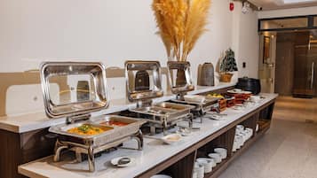 A buffet setup with multiple serving stations, a decorative vase with pampas grass, and a small ship model on the counter.