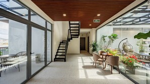 Un interior moderno con una escalera en espiral, paredes de vidrio y un área de comedor con plantas.