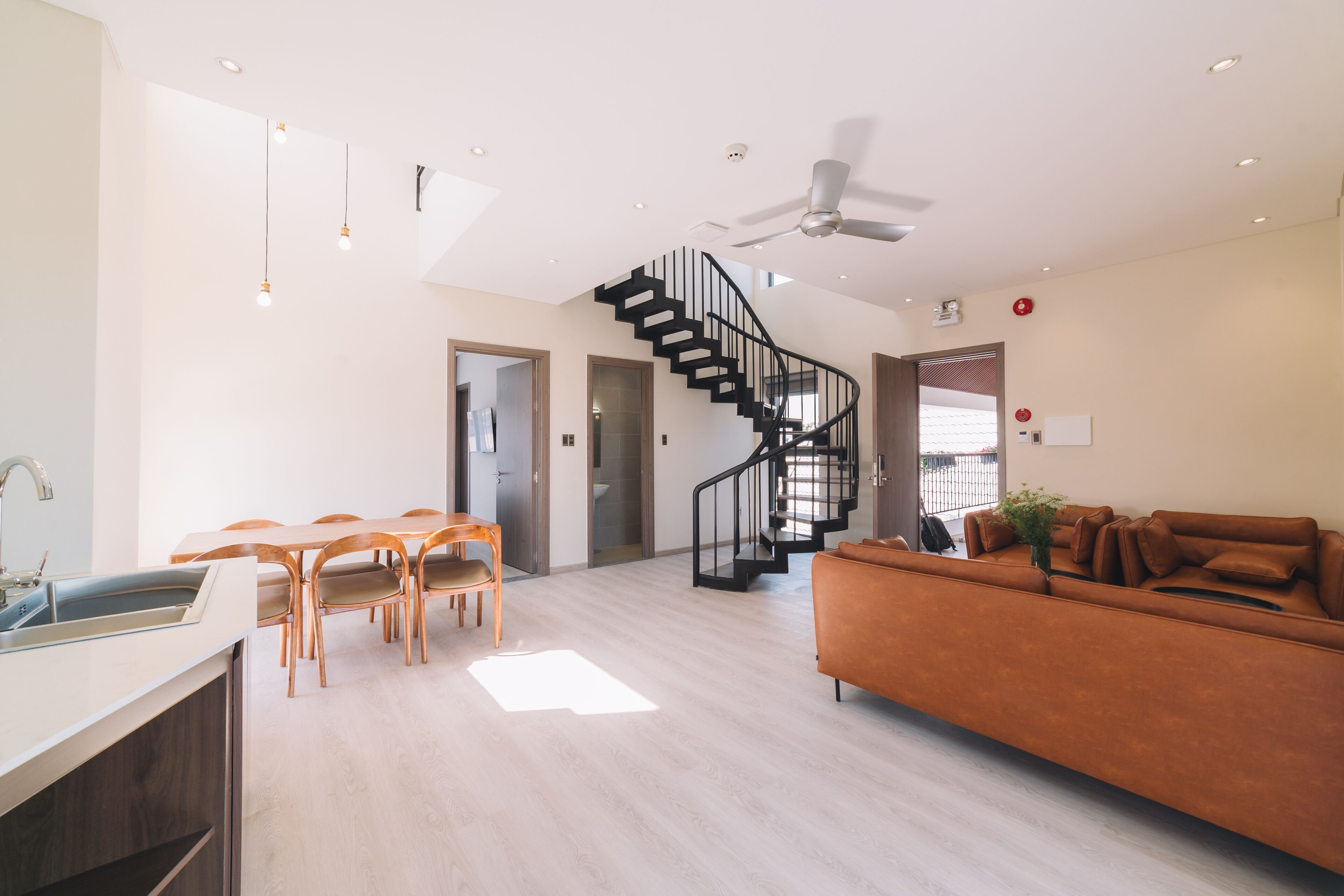 A spacious living area with a staircase, a sofa, a dining table with chairs, and a kitchen area.