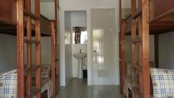 A narrow hallway with a sink and mirror on one wall, flanked by wooden bunk beds with plaid bedding.