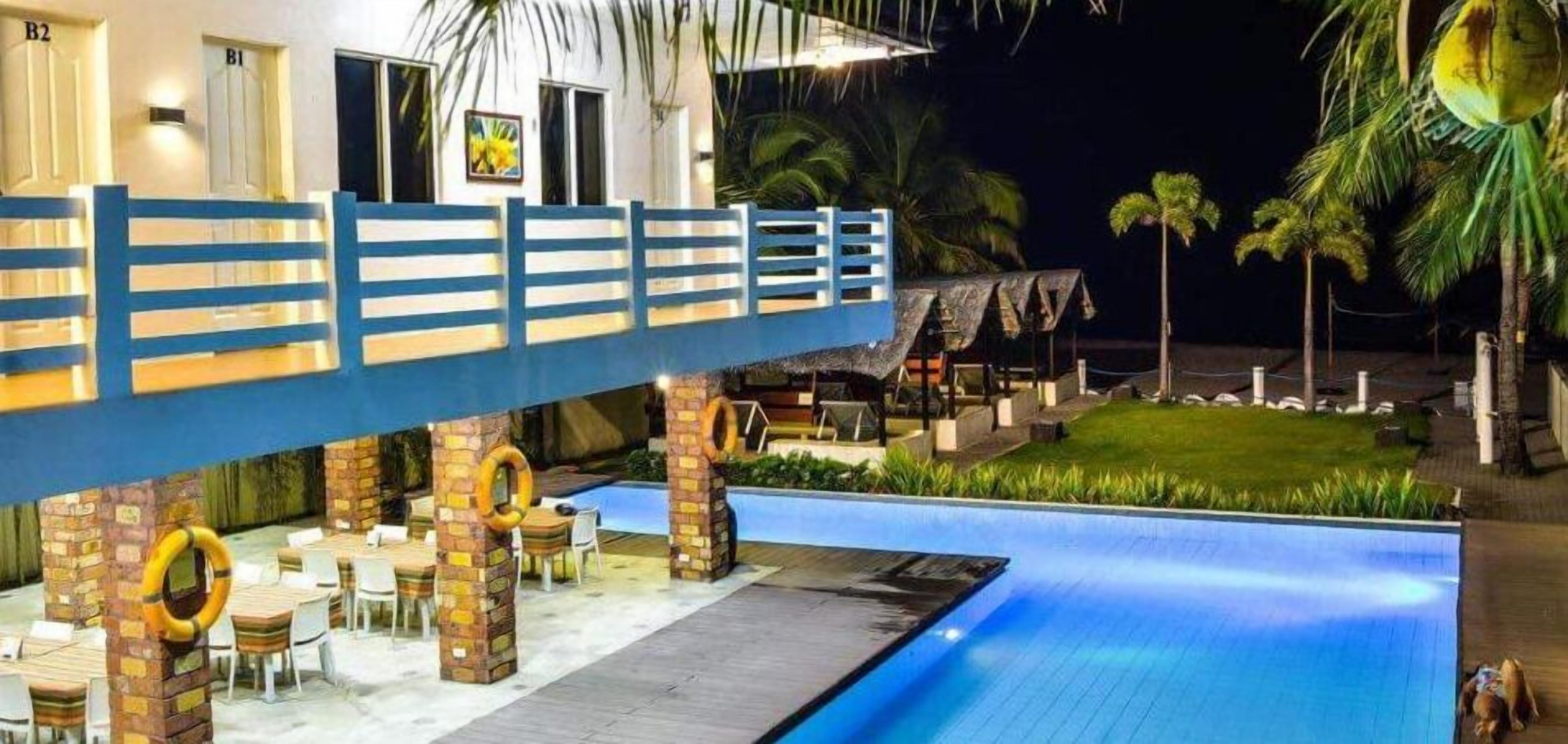 A poolside area with a blue pool, outdoor seating, and palm trees.