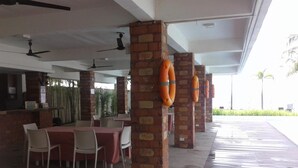 A covered outdoor dining area with brick pillars, tables with red tablecloths, and ceiling fans. - Brizo Hotel and Beach Resort (Morong)