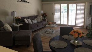 Ein Wohnzimmer mit einer Couch, Sesseln, einem Couchtisch und einem Esstisch mit Unterlagen.