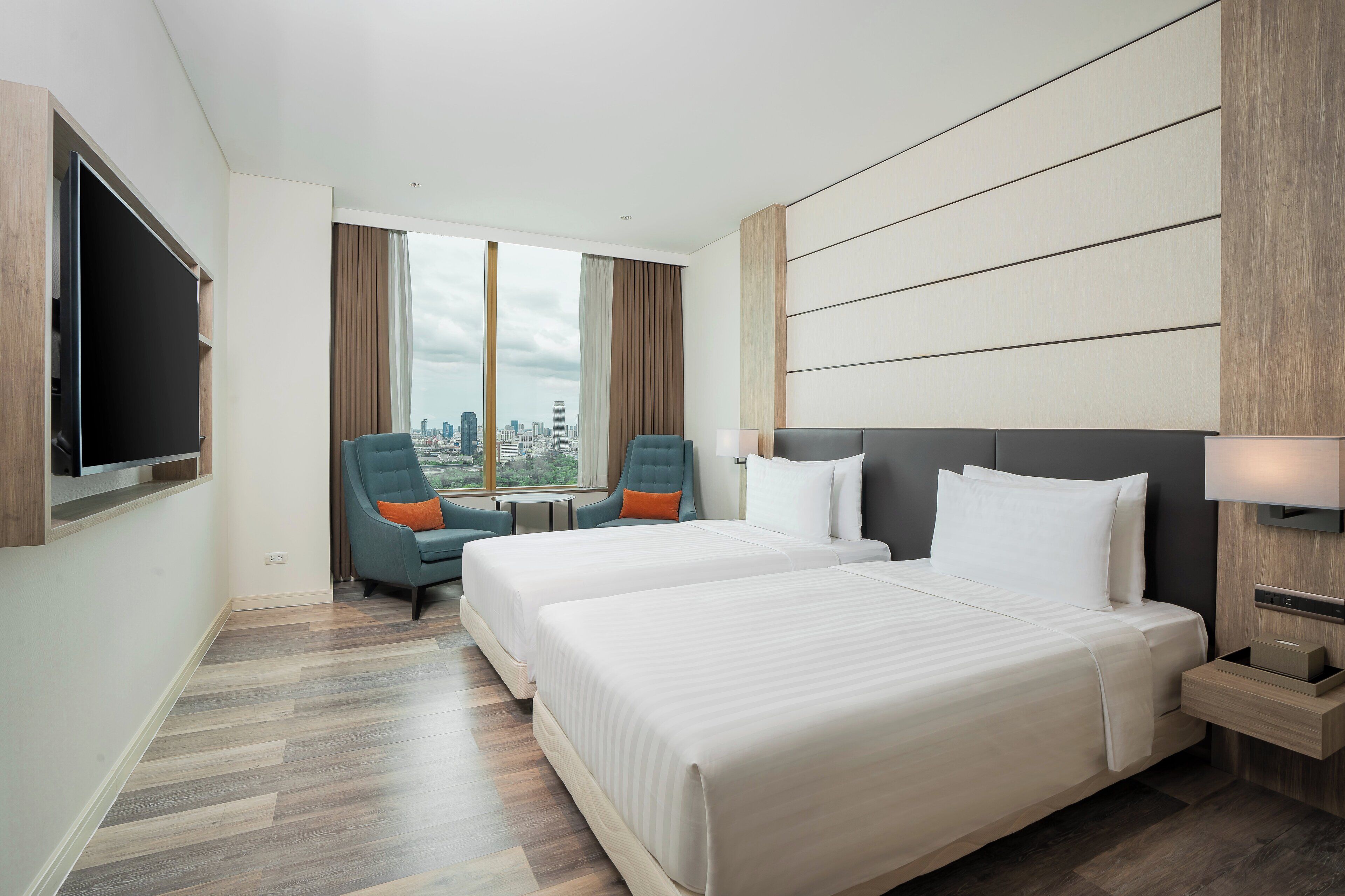 A hotel room with two beds, a TV, a city view, and a cityscape visible through the window.