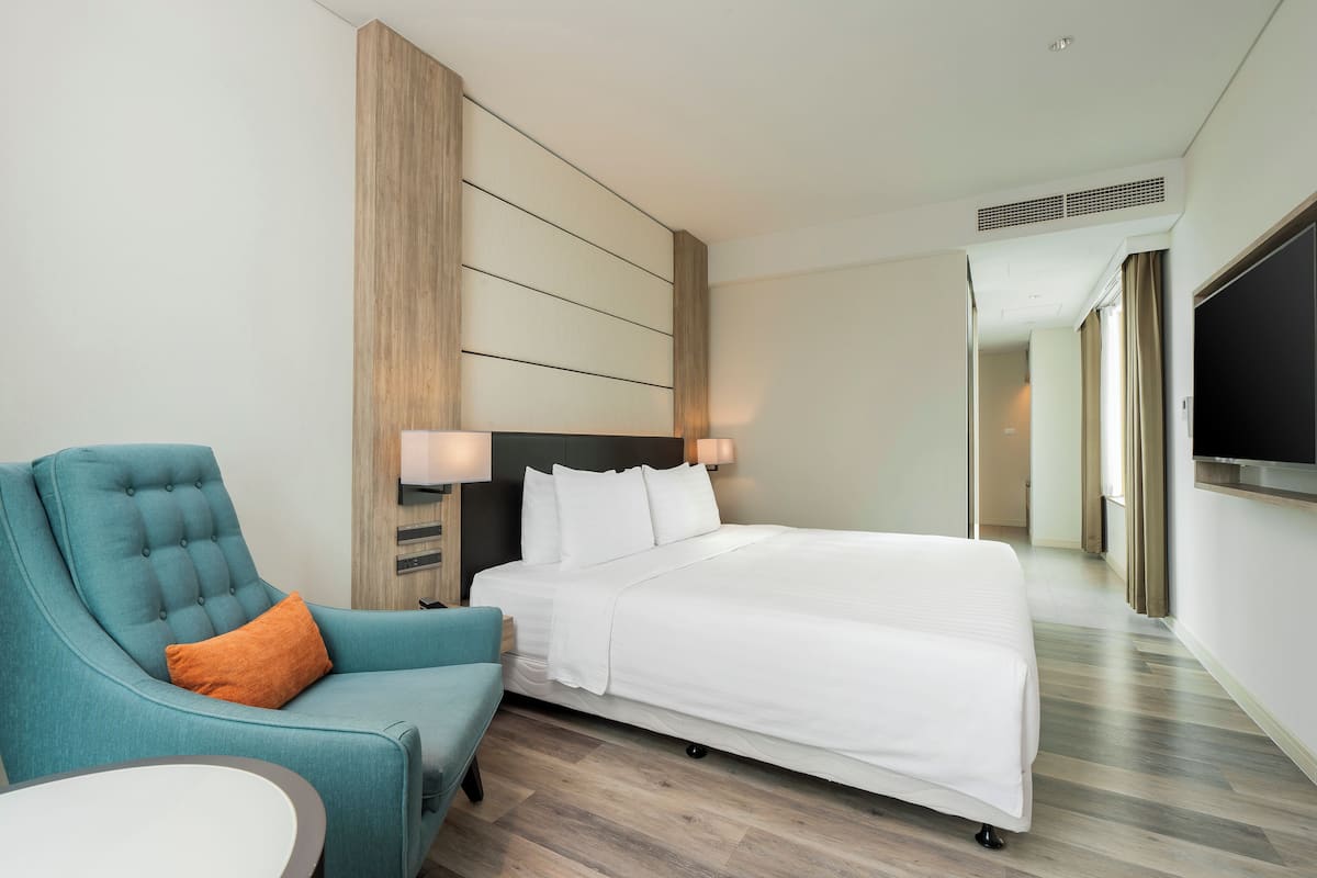 Ein Hotelzimmer mit einem Bett, einem blauen Sessel, einem weißen Sofa und einem Fernseher an der Wand.