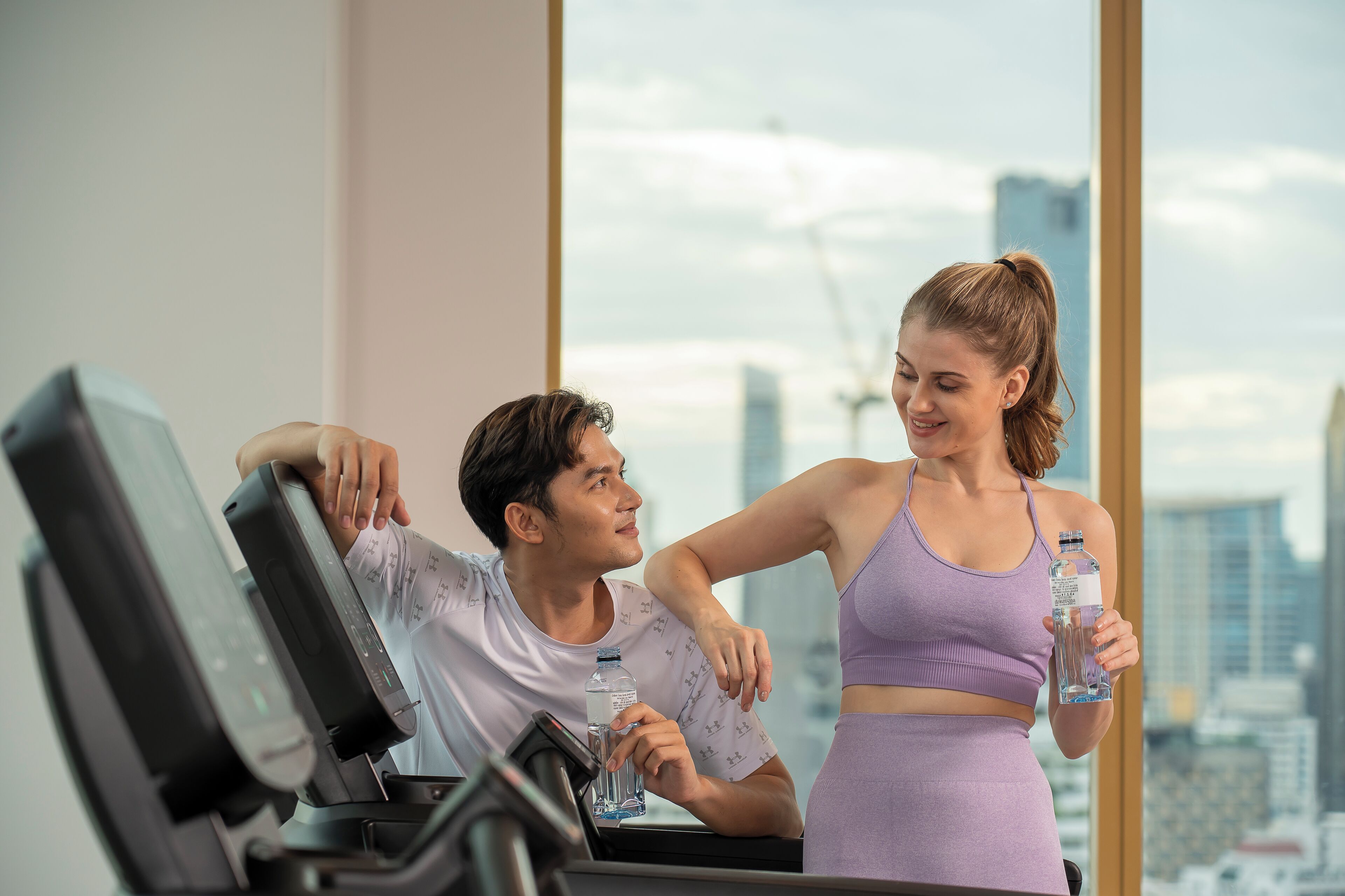 A gym with a treadmill and a city view through large windows.