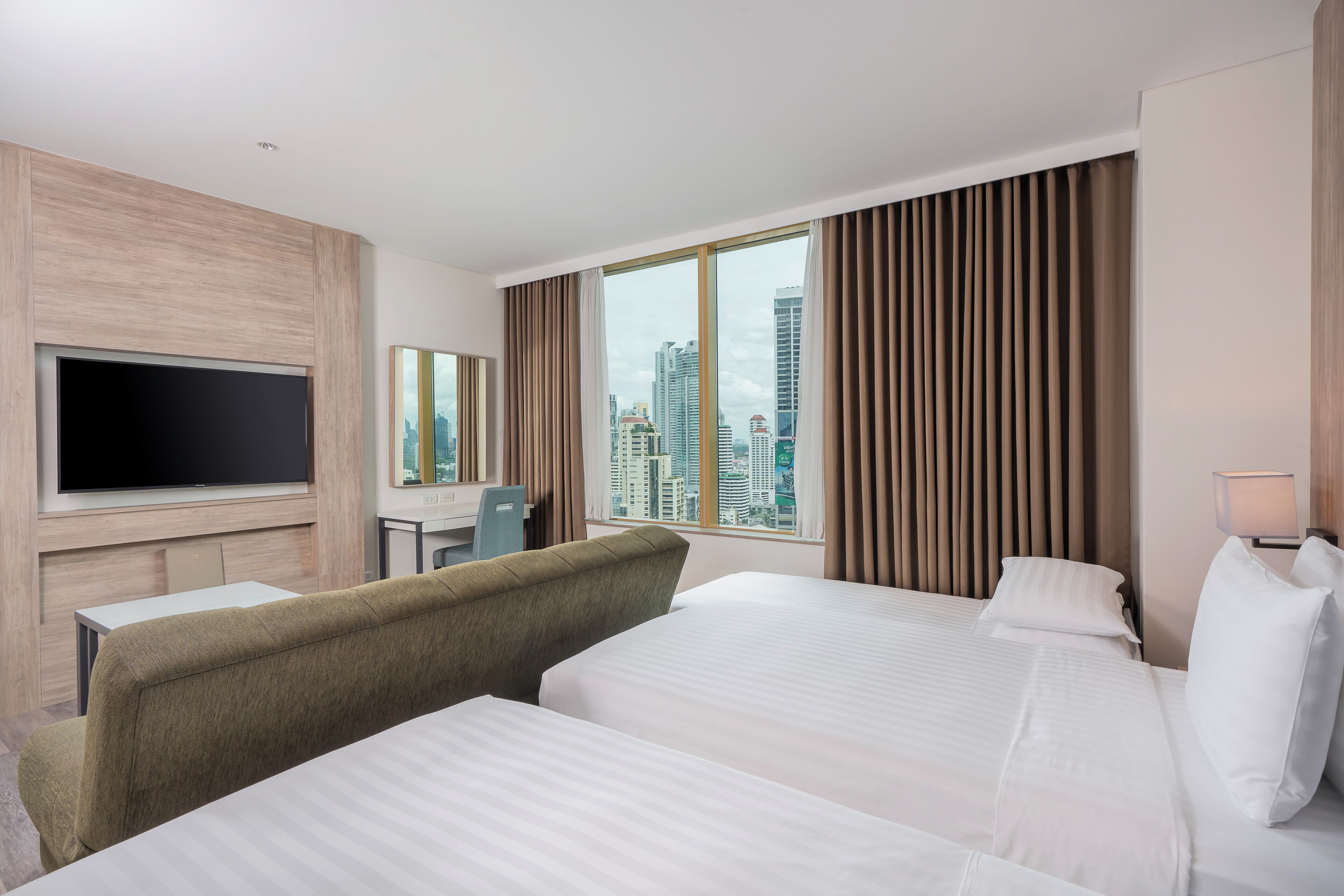 A hotel room with two beds, a TV, a desk, and a city view.