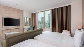 A hotel room with two beds, a TV, a desk, and a city view.
