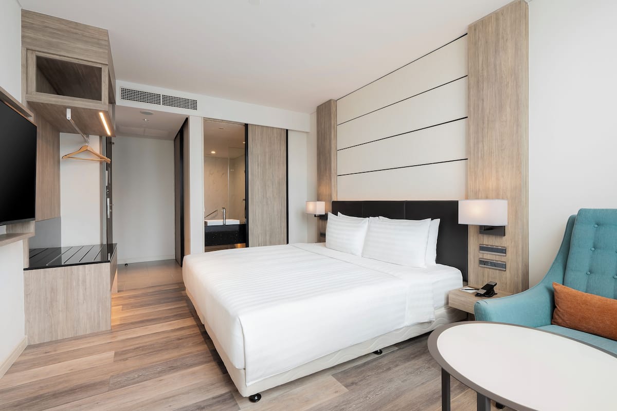 Ein modernes Hotelzimmer mit einem großen Bett, einer Sitzecke mit Tisch, einem Fernseher und einem Kleiderschrank.