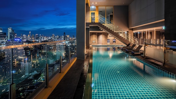 Une piscine à débordement intérieure avec vue sur la ville, un escalier et des chaises longues.