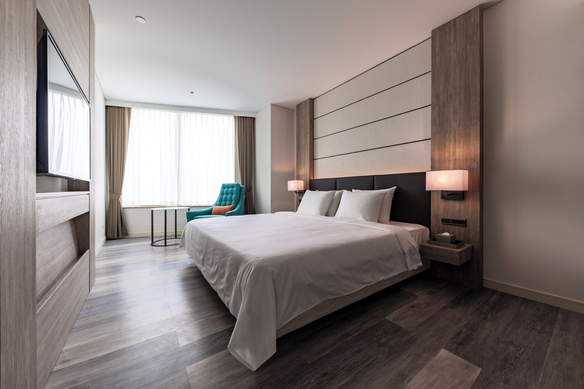 A hotel room with a large bed, a chair, a TV, and a desk.