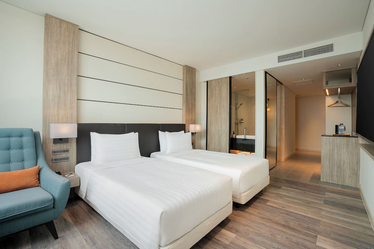 Ein Hotelzimmer mit zwei Betten, einer Sitzecke, einem Spiegel und einem durchgehenden Türrahmen sichtbaren Badezimmer.