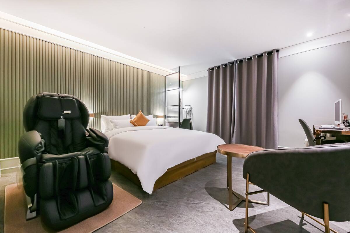 A hotel room with a bed, a massage chair, a desk, and a chair.