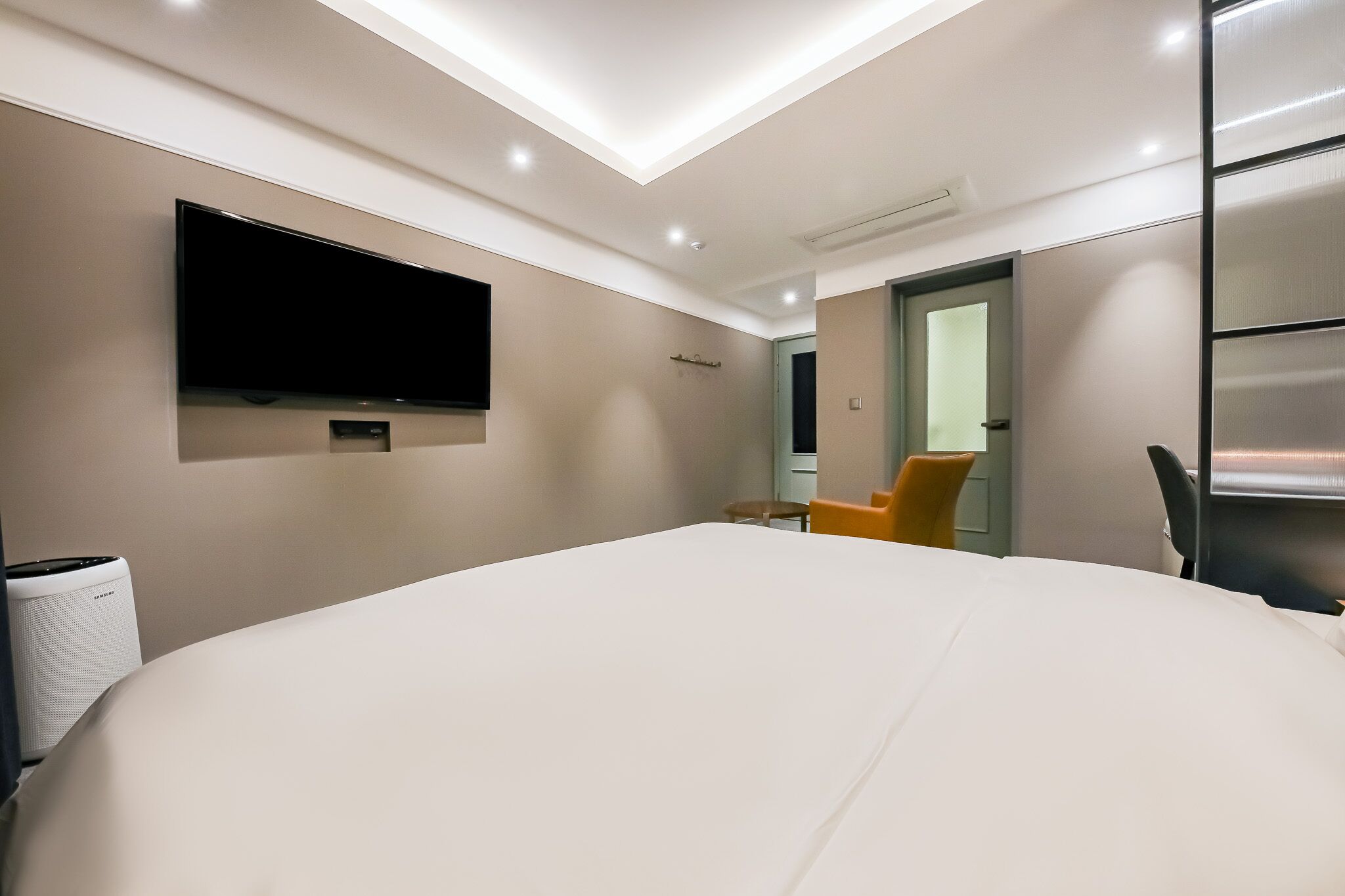 Une chambre d’hôtel moderne avec un grand lit, un téléviseur à écran plat fixé au mur, une petite table et une chaise.