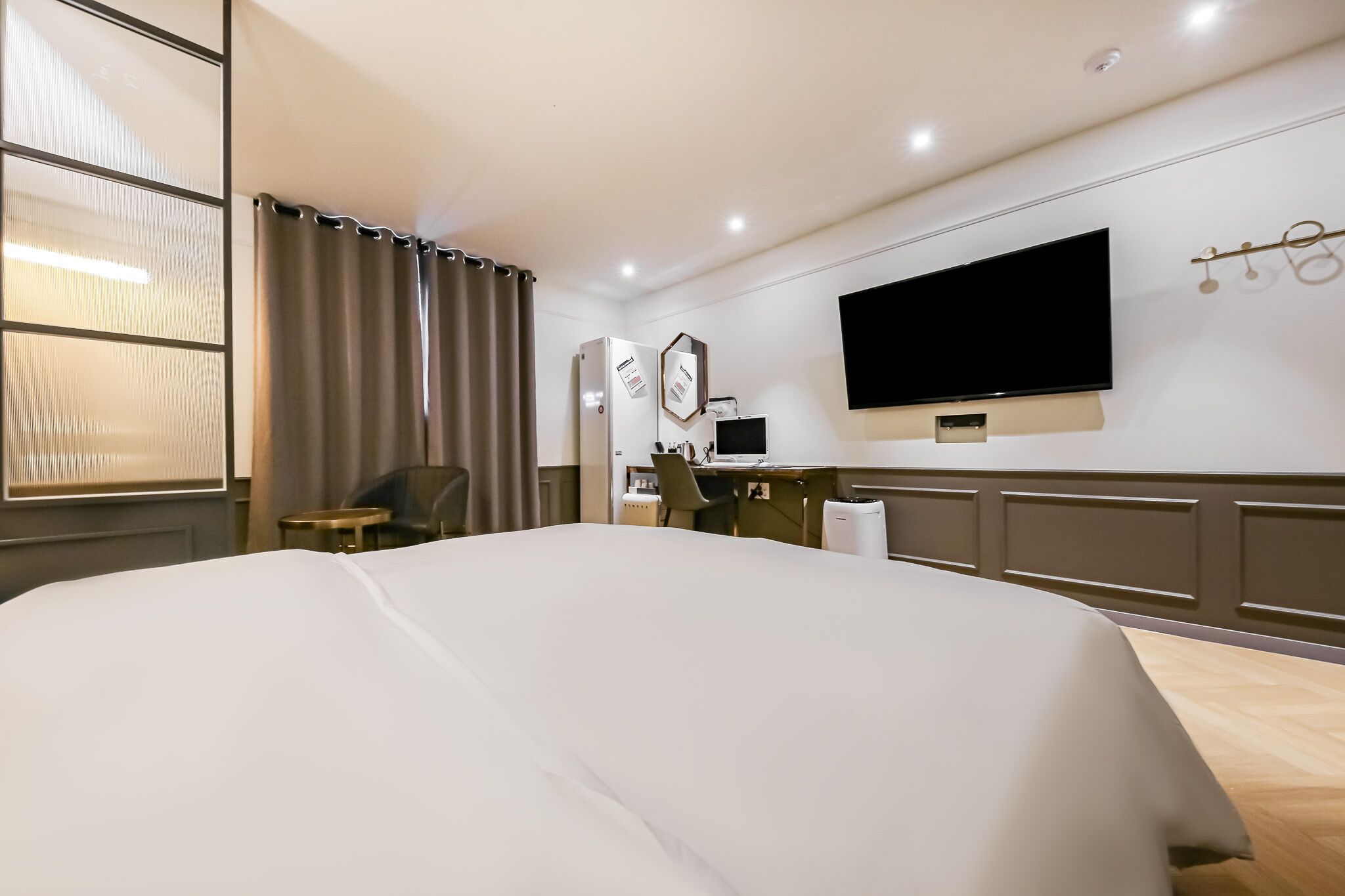 Habitación de hotel con una cama grande, un escritorio con computadora, un televisor de pantalla plana y una ventana con cortinas.