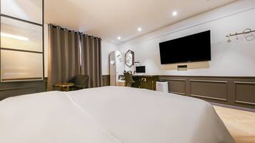 Habitación de hotel con una cama grande, un escritorio con computadora, un televisor de pantalla plana y una ventana con cortinas.