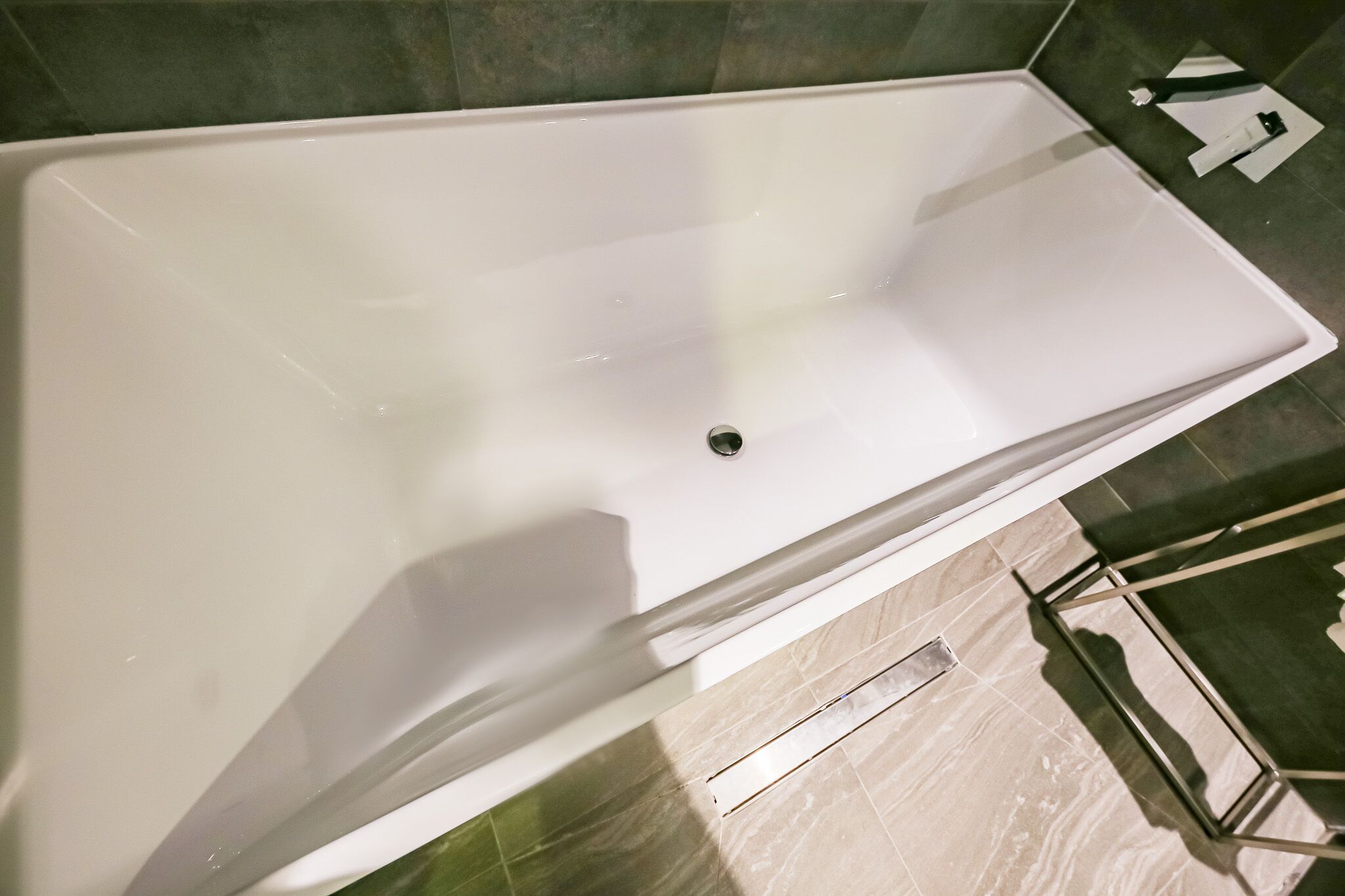 A large, empty bathtub with a drain in the center, surrounded by dark tiles.